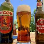 Eine Flasche Picon, ein Glas mit Picon Bière und daneben eine Flasche Kölsch vor blauem Himmel.