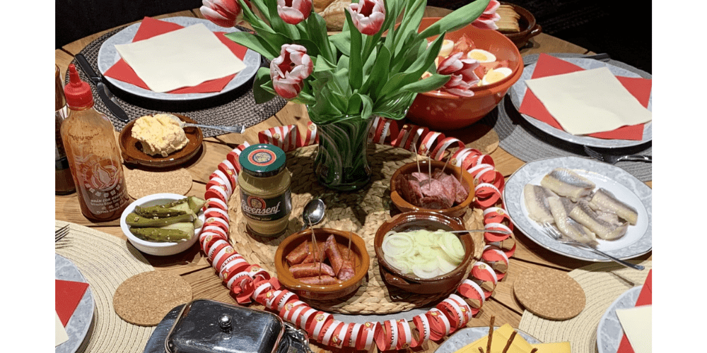 Ein gedeckter Holztisch mit rot und weißer Dekoration und einem Strauß rot-weiße Tulpen in der Mitte. Dazu ein paar kleine Vorspeisen aus Köln unter dem Motto Kölsche Tapas.