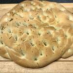 Ein Focaccia auf einem Holzbrett. Das ligurische Fladenbrot ist mit Salz und gehackten Kräutern bestreut und sieht sehr lecker aus.