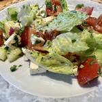Ein griechischer Bauernsalat mit Salat, Tomate, Zwiebeln, Feta sowie Dressing und wiebeln auf einem weißen Porzellanteller mit grau gemustertem Rand.
