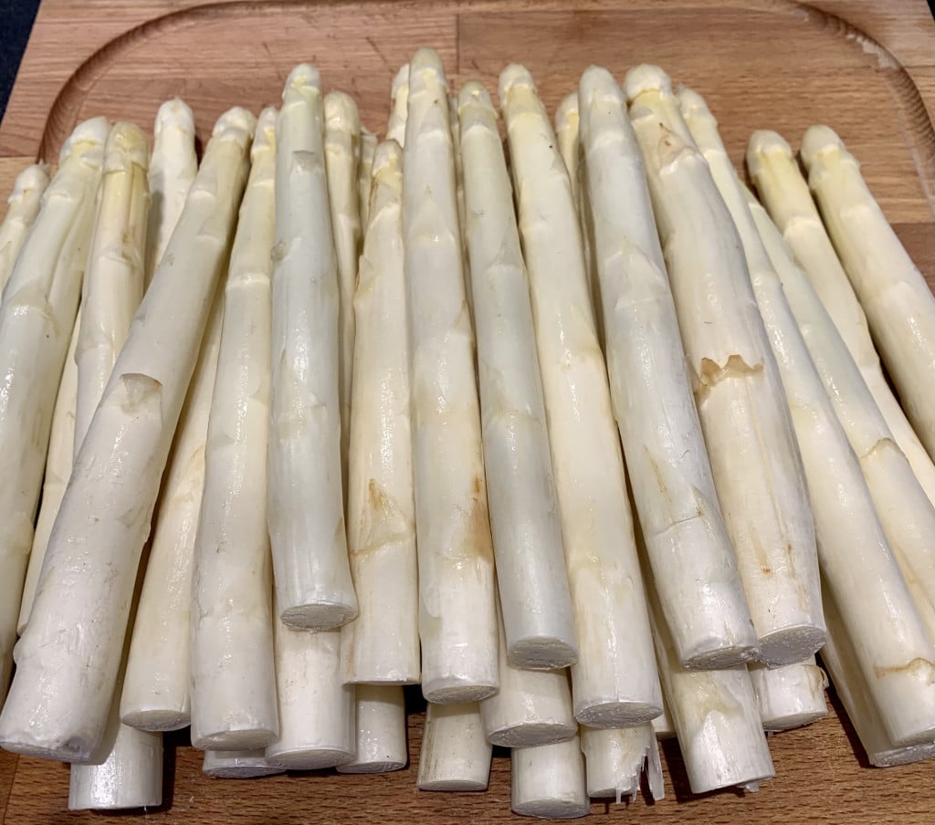 mehrere Stangen weißer, ungeschälter Spargel auf einem Holzbrett in der Küche.