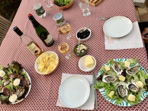 Ein gedeckter Tisch in Aubenas an der Ardèche. Auf einer rot gemusterten Decke sieht man verschiedene Speisen, zwei Flaschen Wein, ein Teller mit geöffneten Austern, Butter und zwei Tellern.