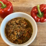 Mexikanische Hühnchen Marinade in einer weißen Porzellanschüssel auf einem Holzbrett, daneben zwei rote Paprika.