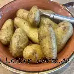 In einer pastell-roten Porzellanschale liegen elf Pellkartoffeln und eine dreizackige Kartoffelgabel.