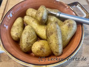 In einer pastell-roten Porzellanschale liegen elf Pellkartoffeln und eine dreizackige Kartoffelgabel.