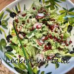 Eine Salatschüssel mit einem bunten Salat, Radieschen und Granatapfelkernen sowie grünem Salatbesteck.