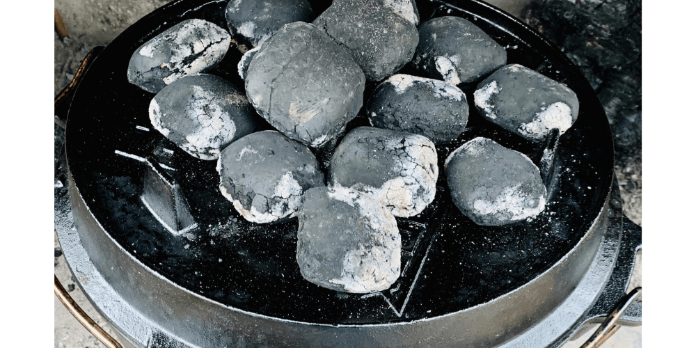 Ein Dutch Oven (Dopf) in einer Feuerstelle. Auf dem Deckele liegen 14 glühende Kohlen.