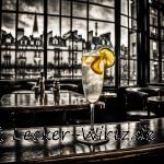 Ein Cocktail mit Eiswürfeln und Zitronenscheiben in einem Sektglas auf einer Bartheke mit blick auf ein Fenster. Im Hintergrund nahezu schwarz weiß eine Häuserzeile verschwommen und davor Tische und Stühle aus der Bar.