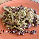 Auf einem roten Teller sind grüne Bohnen. Kidneybohnen und Bratwurst scheiben untereinander angerichtet.