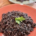 Ein roter Teller mit gekochten, schwarzen, Beluga Linsen und einem Blatt Petersilie