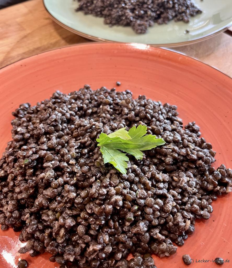 Ein roter Teller mit gekochten, schwarzen, Beluga Linsen und einem Blatt Petersilie