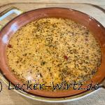 Ein roter Suppenteller mit Henkeln auf einer Holzplatte darin befindet sich eine griechische Feta Suppe