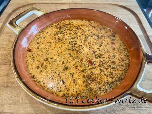 Ein roter Suppenteller mit Henkeln auf einer Holzplatte darin befindet sich eine griechische Feta Suppe