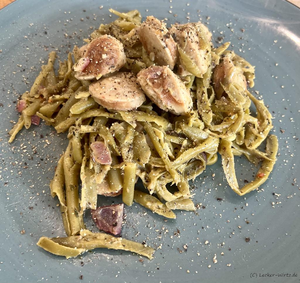 Auf einem blauen Teller sind Schnibbelbohnen mit Bratwurst angerichtet.
