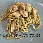 Auf einem blauen Teller sind Schnibbelbohnen mit Bratwurst angerichtet.