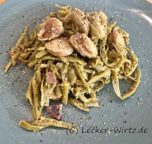 Auf einem blauen Teller sind Schnibbelbohnen mit Bratwurst angerichtet.