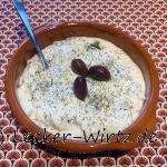 Eine irdene Tonschüssel (Cazuela) mit Tzatziki. Bestreut mit Dill und drei schwarzen Oliven garniert.