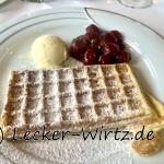 Eine Bergische Waffeln, bestreut mit Puderzucker, mit heißen Kirschen und Vanilleeis auf einem weißen Porzellanteller.