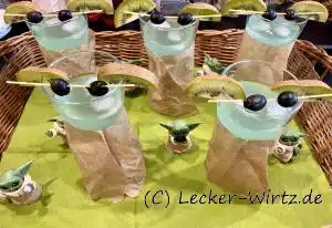 Eicn mint-grüner Cocktail in einem Cocktaikelch, der mit einem Stück braunen Papier umwickelt ist. Zwei halbe Kiwischeiben und zwei schwarze Oliven auf einem Spaghetti geben den Cocktail eine Note von Yoda aus Star Wars. May the force be with you! - may the forth