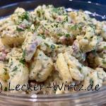 Ein Pfälzer Grumbeersalat (Kartoffelsalat) mit Speck, gehackter Petersilie und Zwiebelstückchen in einer Glasschale.
